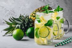 two mason jars filled with lemonade and limes next to some pineapples