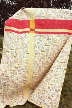 a quilted blanket sitting on top of a grass covered field