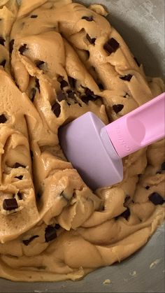 a mixing bowl filled with batter and chocolate chip cookie dough, with a pink spatula in it