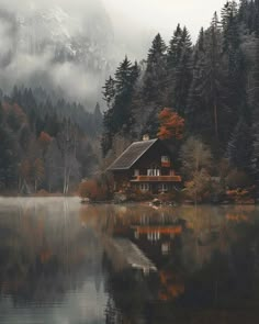 a cabin on the shore of a lake surrounded by trees and foggy mountains in the background