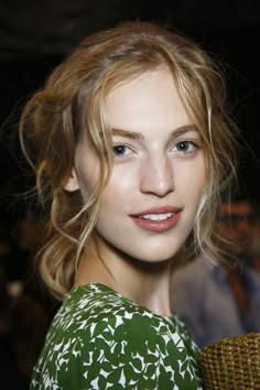 a close up of a person wearing a green and white dress with wavy hair, smiling at the camera