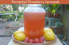 a glass jar filled with liquid sitting on top of a table next to lemons and strawberries