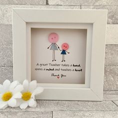 two pink and blue dolls in a white frame next to a flower on a gray brick wall