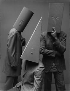 two men in suits with hats on their heads and one man holding a large object