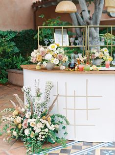 an outdoor bar with flowers and candles on the counter, surrounded by greenery in front of a tree