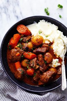 a bowl filled with meat, potatoes and carrots next to mashed potatoes on a striped cloth