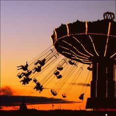 an amusement park ride at sunset with the sky in the backgrouund and silhouettes of people riding on swings