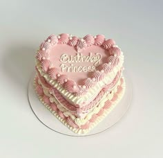 a heart shaped birthday cake sitting on top of a white plate with pink frosting