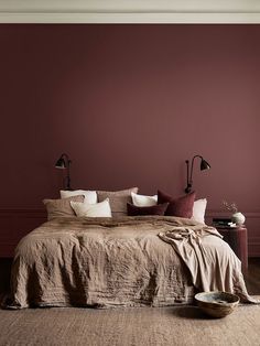 a bed with pillows and blankets on top of it next to a wall painted red