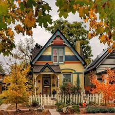 a yellow house with blue trim surrounded by fall foliage and trees in the front yard