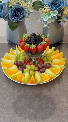 a plate topped with fruit and flowers next to two vases filled with blue roses