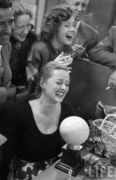 black and white photograph of woman laughing with other people around her at a table in an office setting