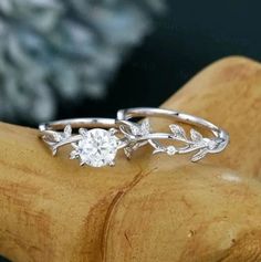 two silver rings with leaves on them sitting on top of a wooden stand in front of a stone wall