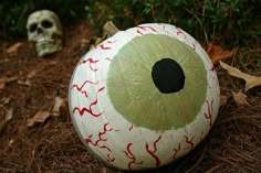 a pumpkin with an eyeball painted on it sitting in the grass next to a skull