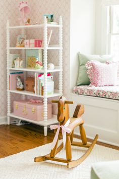 a wooden rocking horse sitting on top of a rug in front of a book shelf