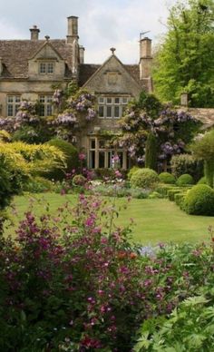 a large house with lots of flowers in the front yard and bushes around it on either side