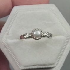 a close up of a person's hand holding a ring with a pearl in it