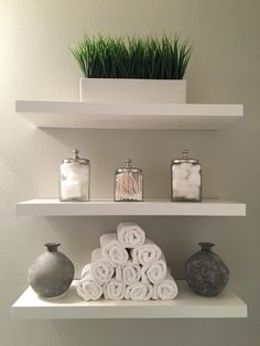 three white shelves with towels and vases on them in a small bathroom, one has grass growing out of the top shelf