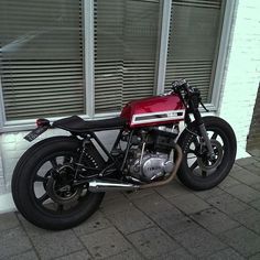 a red and black motorcycle parked in front of a building with shutters on the windows