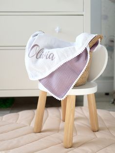 a baby's blanket on top of a wooden stool in a room with white furniture