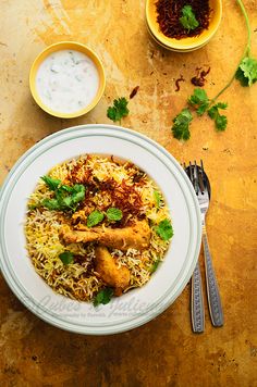 a white plate topped with chicken and rice next to two bowls of sauces on a table