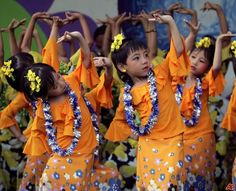 young children in orange and blue outfits dancing with their hands up to the sky while wearing leis