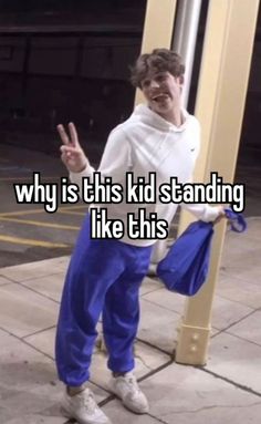 a man in blue pants and white shirt standing next to a pole with the words why is this kid standing like this?