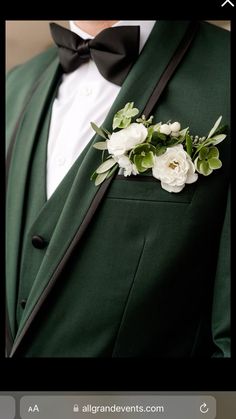 a man wearing a green suit with white flowers in his lapel and black bow tie