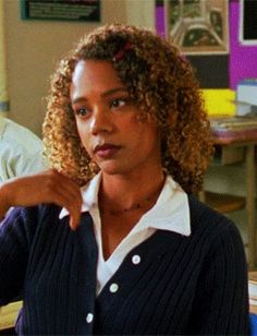 a woman with curly hair sitting at a desk in an office setting and pointing to the side