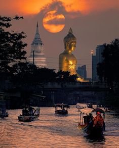 several boats floating in the water with a large buddha statue in the background at sunset