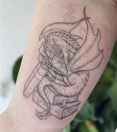 a woman's arm with a tattoo on it that has an image of a dragon holding a book