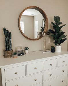 a white dresser topped with a mirror next to a potted plant and a cactus