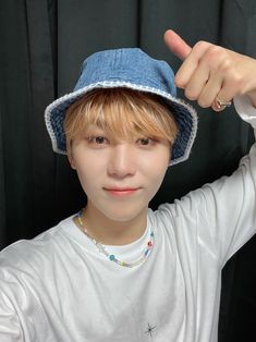 a young man wearing a blue hat giving the peace sign with his hand while standing in front of a black background