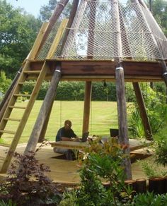 a person sitting on a wooden platform in the middle of a garden with a netted roof