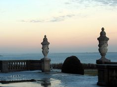 two statues on top of a building next to the ocean at sunset or dawn with clouds in the sky