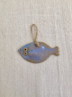 a small blue fish ornament hanging on a white linen background with twine