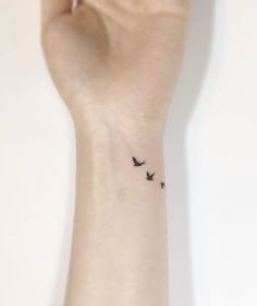 a small tattoo on the wrist of a woman with two birds flying in the sky