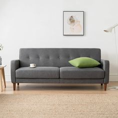 a living room with a gray couch and green pillow on the floor next to a lamp