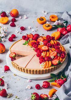 there is a pie with fruit on the top and flowers around it, surrounded by other fruits