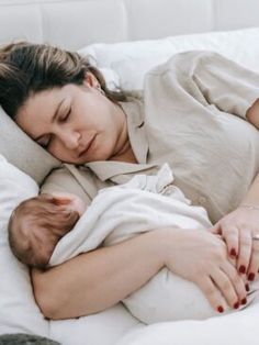 a woman laying in bed with her baby sleeping on it's back and she is wearing a white shirt