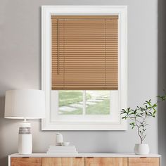 a room with a dresser, lamp and window covered in blinds on the windowsill