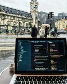 an open laptop computer sitting on top of a wooden table in front of a building