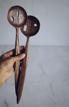 two wooden spoons with faces on them are held up by someone's hand