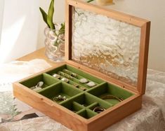 an open wooden box with rings inside on a table next to a vase and flowers