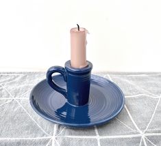 a blue cup and saucer with a pink candle on it sitting on a gray tablecloth