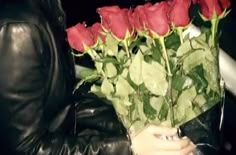 a man holding a bunch of red roses in his hand and wearing a black leather jacket