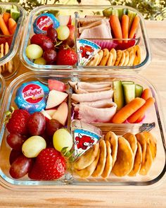 three plastic containers filled with food on top of a wooden table next to fruit and veggies