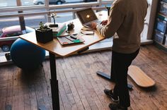 a man standing in front of a laptop computer on top of a wooden desk next to a window