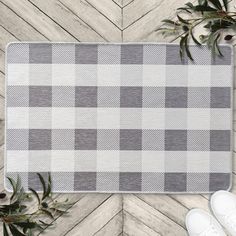 a gray and white checkered rug on top of a wooden floor next to sneakers