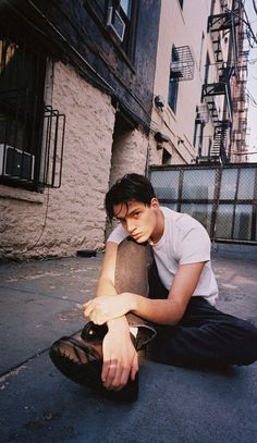 a young man sitting on the ground with his hand on his knee and looking down